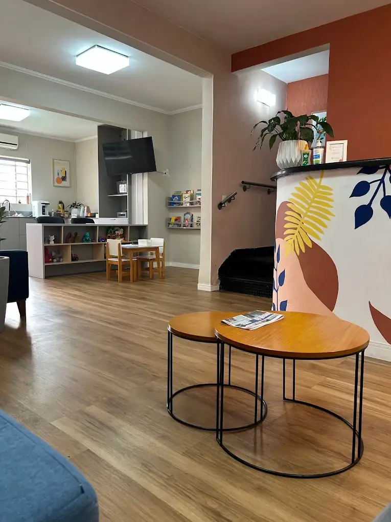 Sala de espera da unidade Pio XI, com mesinhas redondas, o mural de folhas e o cantinho das crianças ao fundo