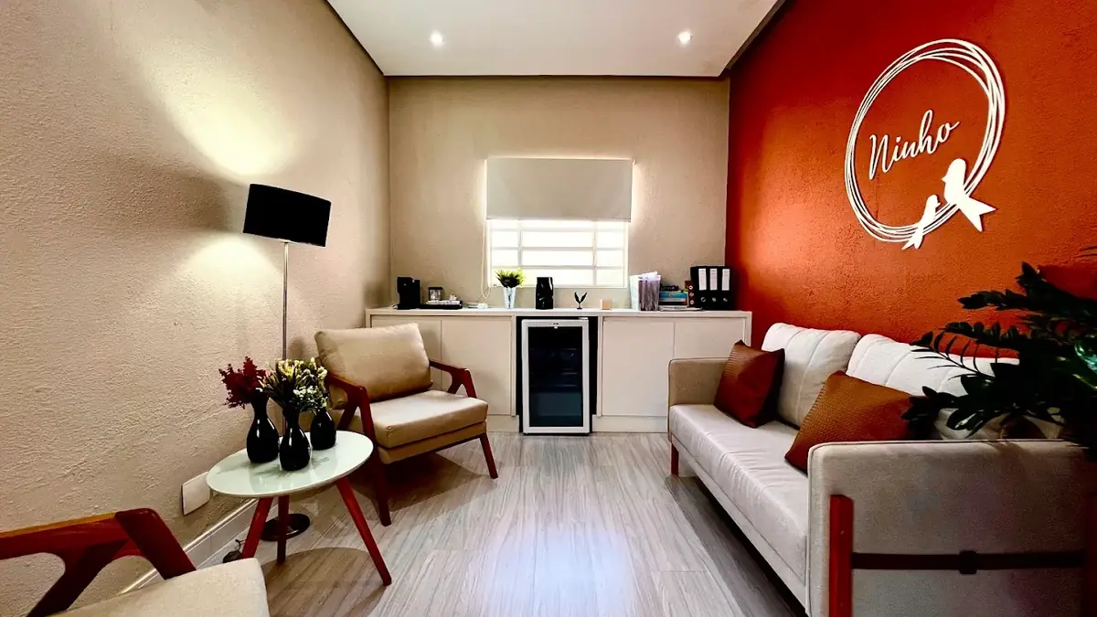 Sala de estar da unidade Pio XI, com sofá, poltronas e o logo do Ninho na parede terracota